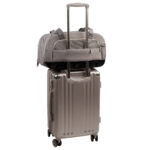 back view of compact, gray pet car seat with two carry handles on top sitting on a silver, hardshell suitcase, secured with the carrier's trolley sleeve - view 6