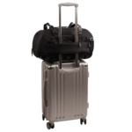 back view of compact, black pet car seat with two carry handles on top sitting on a silver, hardshell suitcase, secured with the carrier's trolley sleeve - view 7