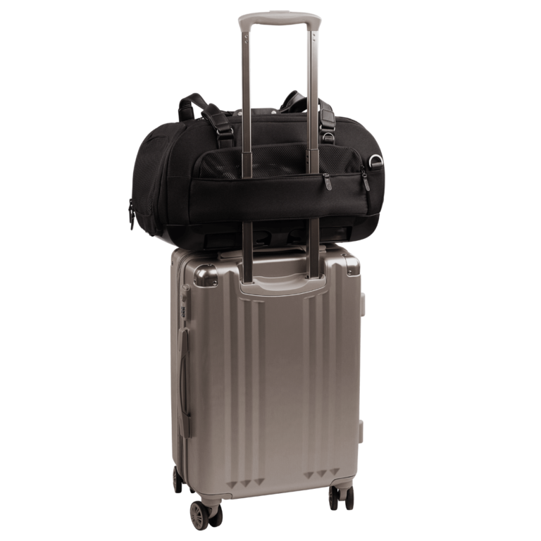 back view of compact, black pet car seat with two carry handles on top sitting on a silver, hardshell suitcase, secured with the carrier's trolley sleeve - view 7
