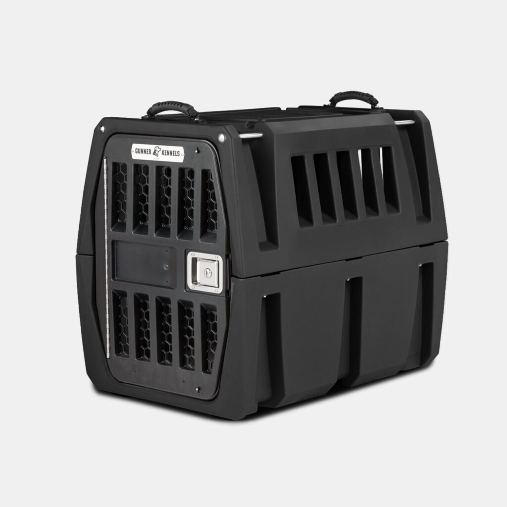 The GUNNER G1™ KENNEL - BLACK is a tough dog crate with sturdy black plastic, a metal mesh door, side ventilation slats, top carrying handles, a secure latch, and reinforced design—ideal for safe pet travel or transport.